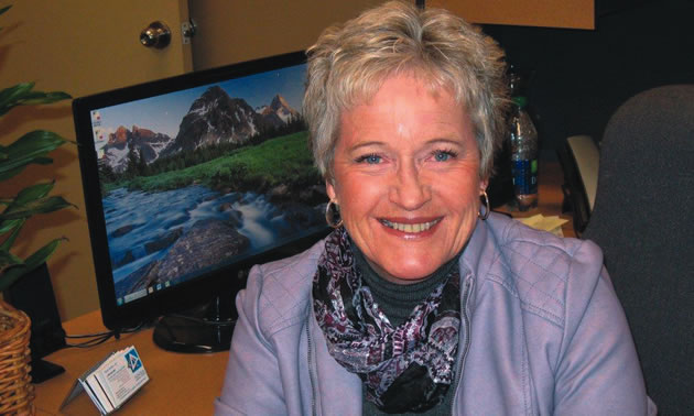 smiling woman with short silver hair at a desk with computer behind