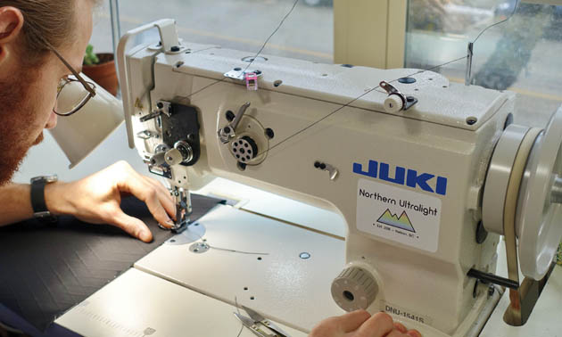 Worker sitting at Juki industrial sewing machine, sewing fabric. 