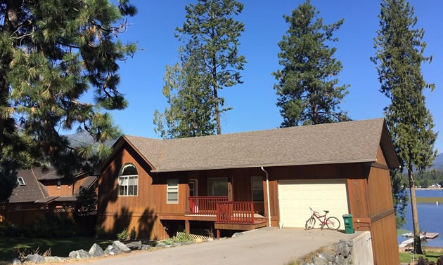 Brown house surrounded by towering pine trees.