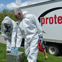 Two staff in hazmat suits stand in front of a truck that reads 