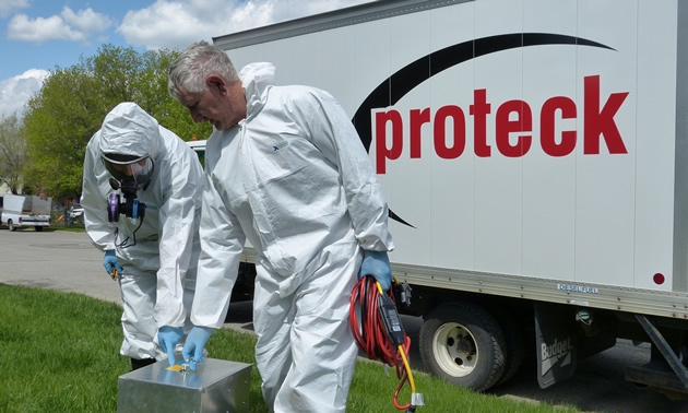 Two staff in hazmat suits stand in front of a truck that reads 