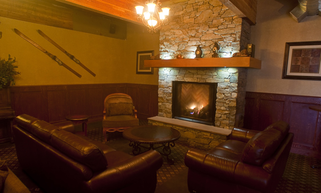 A relaxing atmosphere with a fireplace, comfy brown leather couches and skis on the wall.