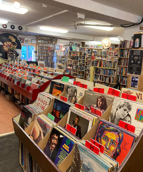 Interior shot of Packrat Annie's, showing long row of books and shelves, records in foreground of picture. 