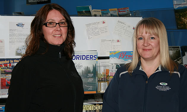 Two women standing in front of brochures at the Chamber of Commerce office in Castlegar.