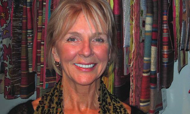 Close-up of smiling, attractive, blonde senior woman, against a background of hanging fabric swatches