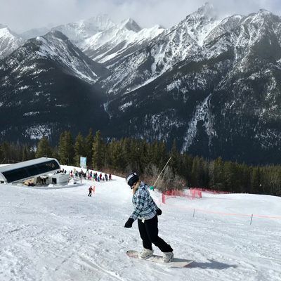 Person snowboarding down hill at Panorama Mountain Resort, wind-swept snowy mountains in background. 