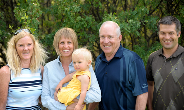 Two women, one holding a toddler, and two men, standing in front of lush greenery