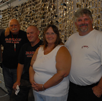 Three employees in black shirts and a couple in white shirts stand in front of a wall covered in key blanks.