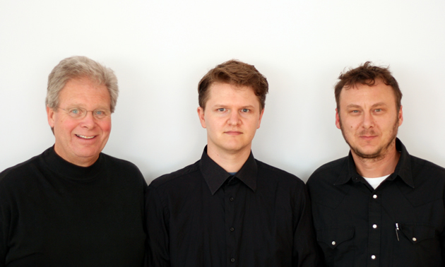 Three men stand next to each other. All wear black shirts.
