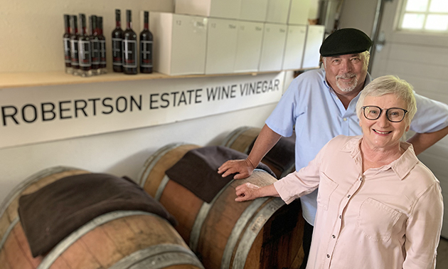 Patrick and Loie Robertson standing beside vinegar barrels. 