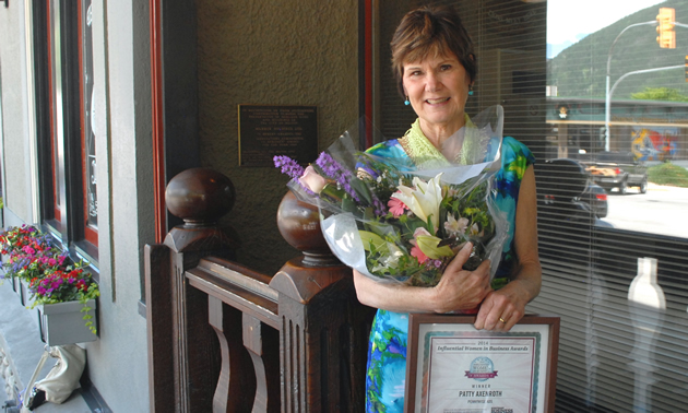 Patty Axenroth stands with a bouquet and a certificate naming her a winner in the West Kootenay Influential Women in Business Awards.