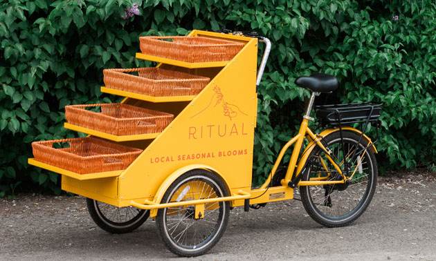 Bright yellow 3-wheeler e-bike with built-in shelves to hold flowers. 