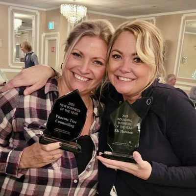 Jennifer Lyall and Erica Latka holding Business Excellence awards and smiling into camera. 