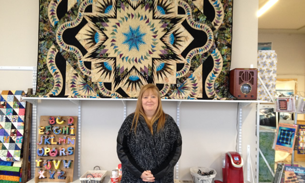 Denise Nagai is standing in front of a beautilful quilt with geometric designs.