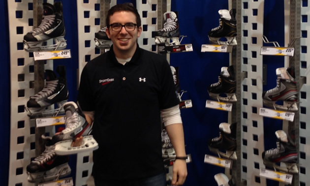 Smiling young man, Ryan Alvernini, standing in front of a large wall display of hockey skates.