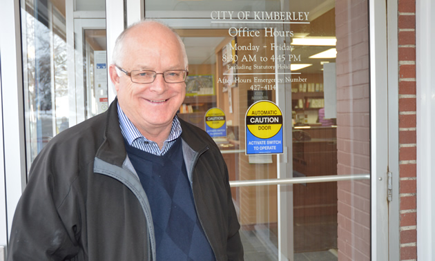 Smiling senior man standing at a glass door bearing the legend 