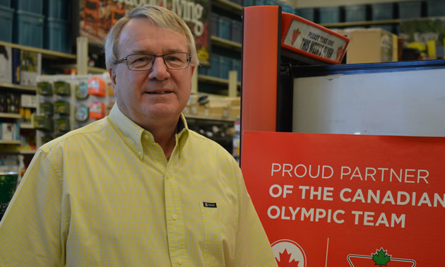 Gray-haired man stands beside a poster promoting Canadian Tire's support of Olympic athletes.