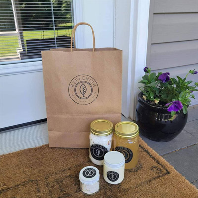 A brown paper bag sitting on a doorstep, with Replenish products arranged in front of the bag. 