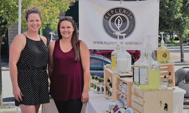 Melinda Nealis and Kayla Carley standing in front of their farmers market booth. 