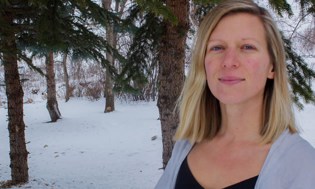 Michelle Tucker is standing next to an evergreen tree in the snow.