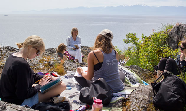 Workshop participants are sitting on a rocky area overlooking the ocean on B.C.'s coastline.
