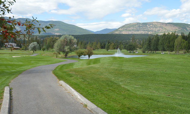 Golf course with shrubs and water hazard, with mountains in the background