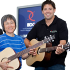 Trio of businessman, Asian woman with guitar and younger man with guitar, smile at camera.
