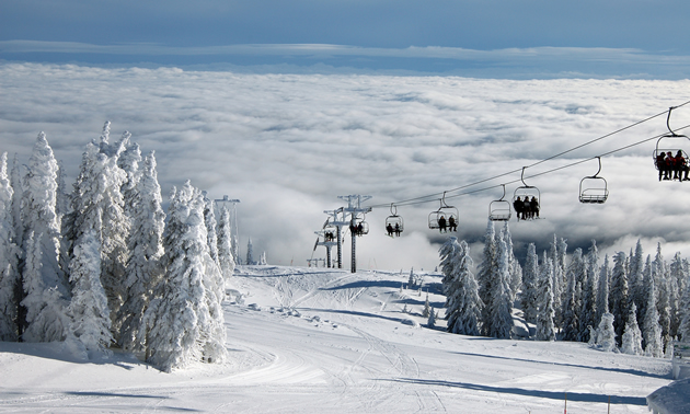 A chair-lift carries skiers up the mountain, apparently through the clouds into sunshine