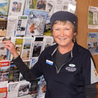 Smiling woman in corporate uniform stands in front of a wall rack of brochures.