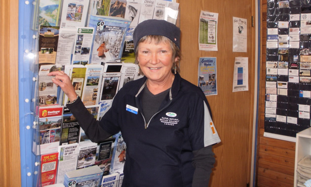 Smiling woman in corporate uniform stands in front of a wall rack of brochures.