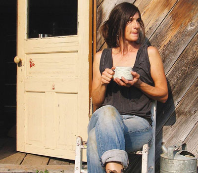 Sarah Pike sitting outside studio, holding mug and looking off into distance. 