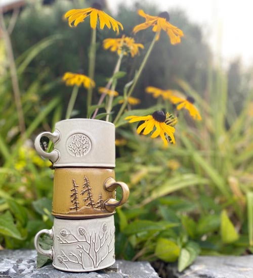 Three mugs sitting atop each other with wildflowers in background. 