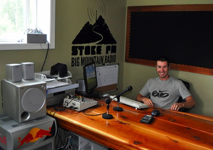 Scott sits behind a wide wood desk and station equipment.