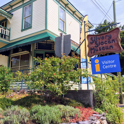 Heritage house painted yellow and green, housing the Slocan Valley Chamber of Commerce and the Silvery Slocan Museum. 