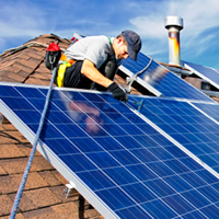 A construction worker affixes solar panels to a roof.