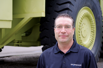 A man stands in front of a giant dump truck