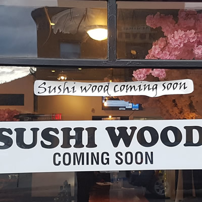 Sign in window advertising the opening of Sushi Wood restaurant. 