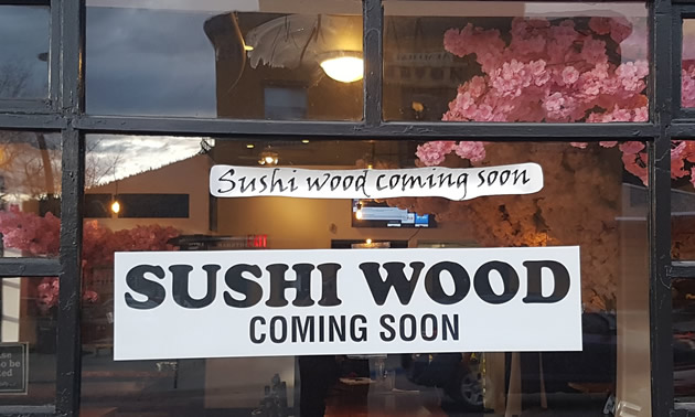 Sign in window advertising the opening of Sushi Wood restaurant. 