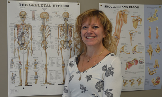 Smiling blonde woman stands in front of anatomical charts