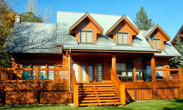 A honey-coloured log home by Trappeur Homes has a green roof, three gables and a porch.