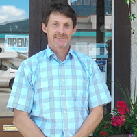 Man in short-sleeved pale blue shirt and dark pants standing outside an open office doorway, outdoors