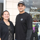 Young middle-aged couple stand in front of a store displaying Trade Your Treasures sign.
