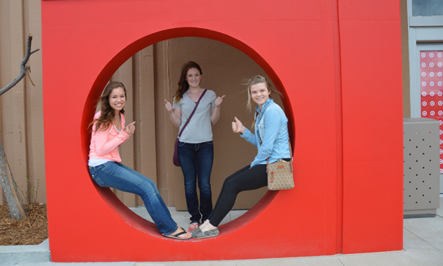 Three teenage girls within a circular cutout in a red-coloured upright square