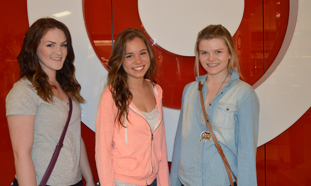Three teenage girls stand in front of a red-on-white target