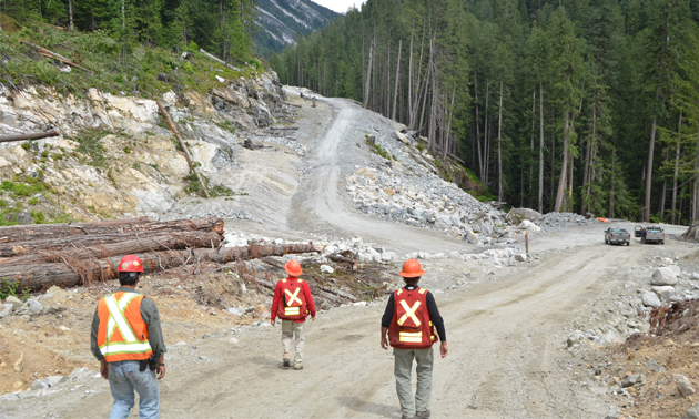 Three workers in safety gear are at their work site on a recently built resource road.