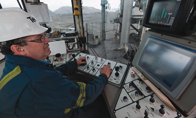 A man wearing a hard hat operating a complex control board with a monitor 