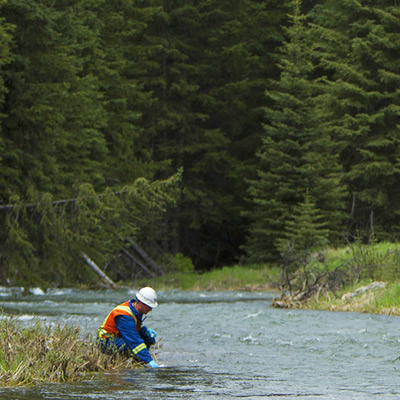 A Teck employee crouched beside a river. 