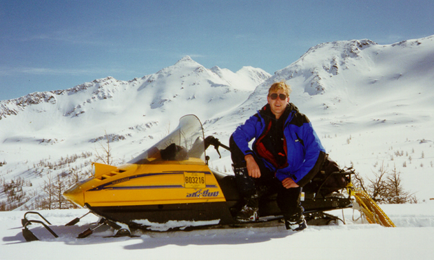 Man with yellow snowmobile on a snow covered mountain