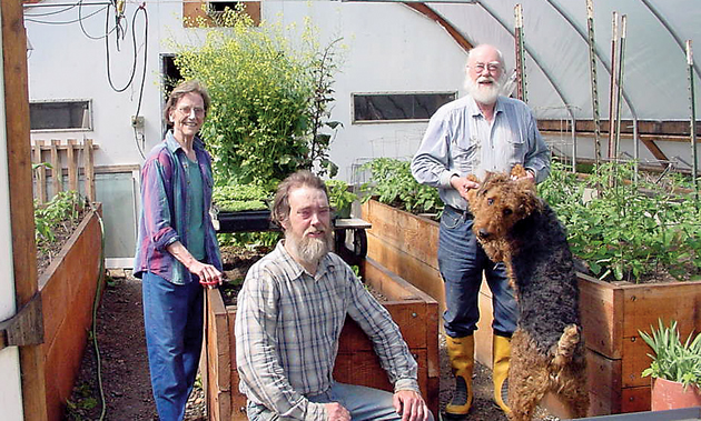 The Haagerup family sits in their greenhouse around plant boxes and smile. Bent is holding the paws of a big dog.