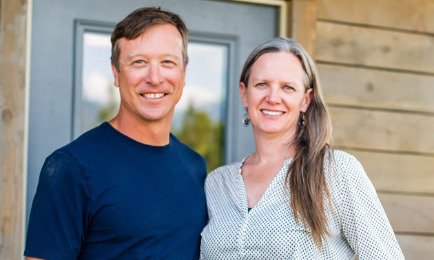 Paul Denchuk and Meredith Hamstead are standing together in front of a home.
